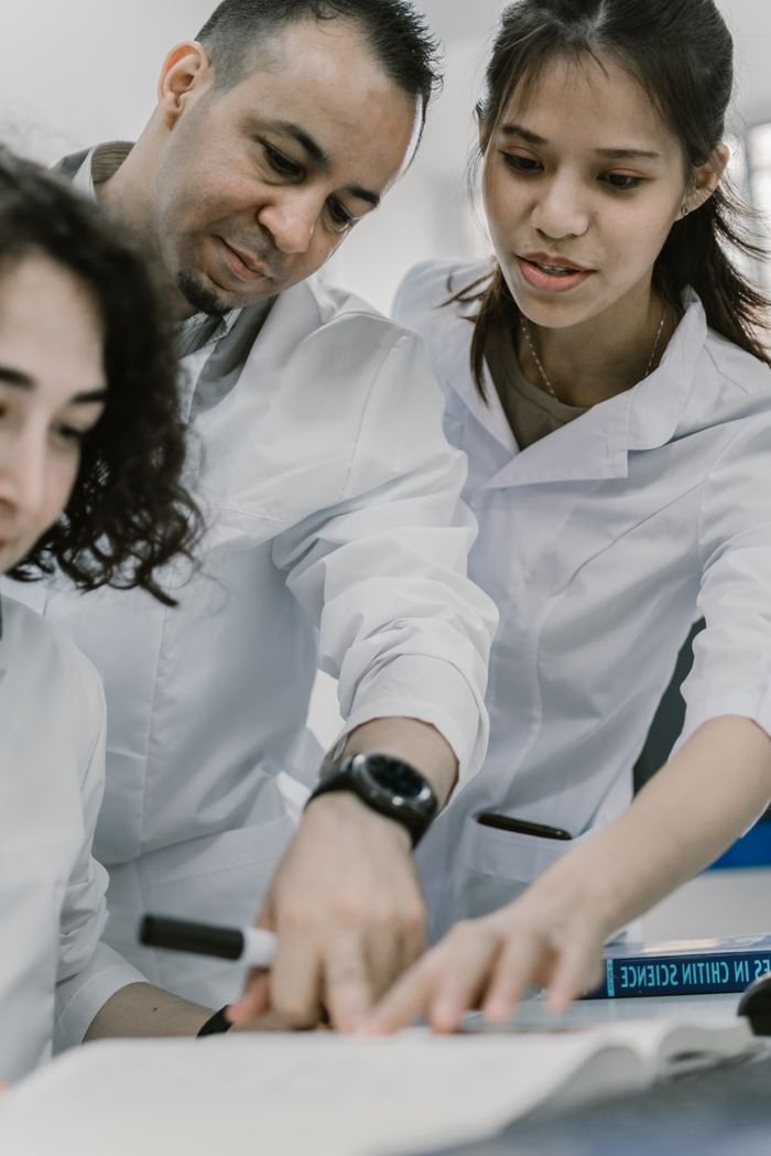 A diverse group of professionals work on a science project, focusing on a book.